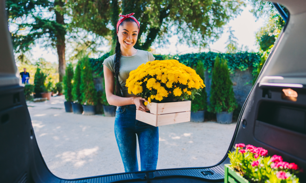 Florist putting box of mums into back of delivery van and smiling at camera