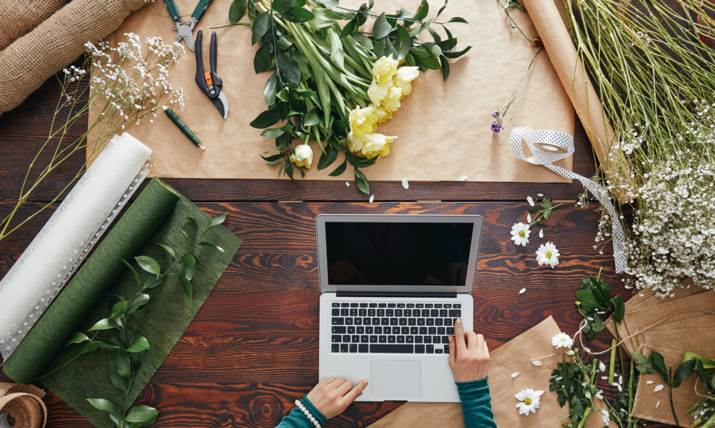 overhead shot of a laptop on a table surrounded by floral supplies