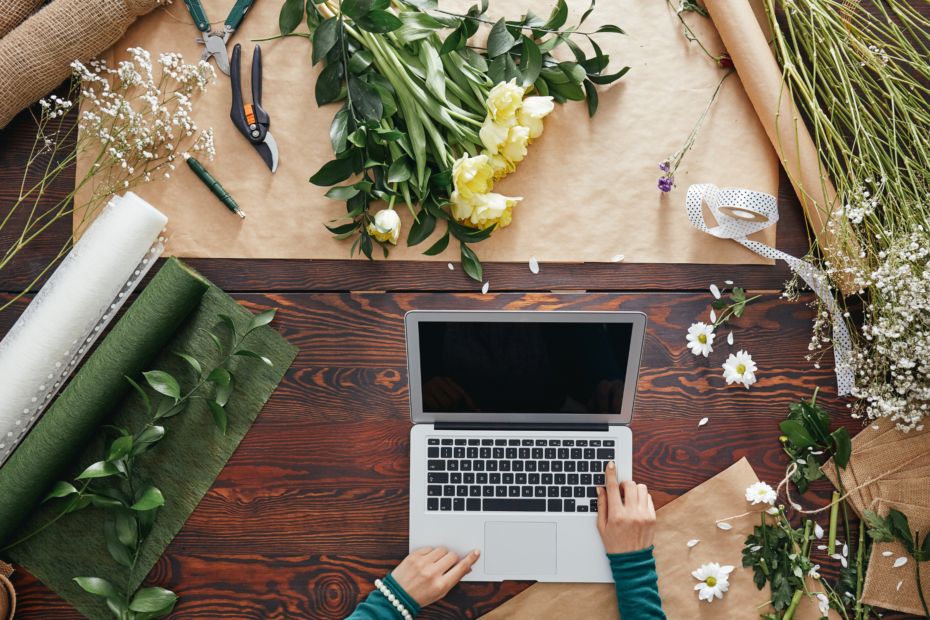 overhead shot of a laptop on a table surrounded by floral supplies